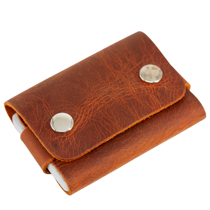 A brown leather card holder wallet with a textured finish, featuring two silver metal snap buttons and a white elastic band visible on the side, set against a plain white background. #Camel