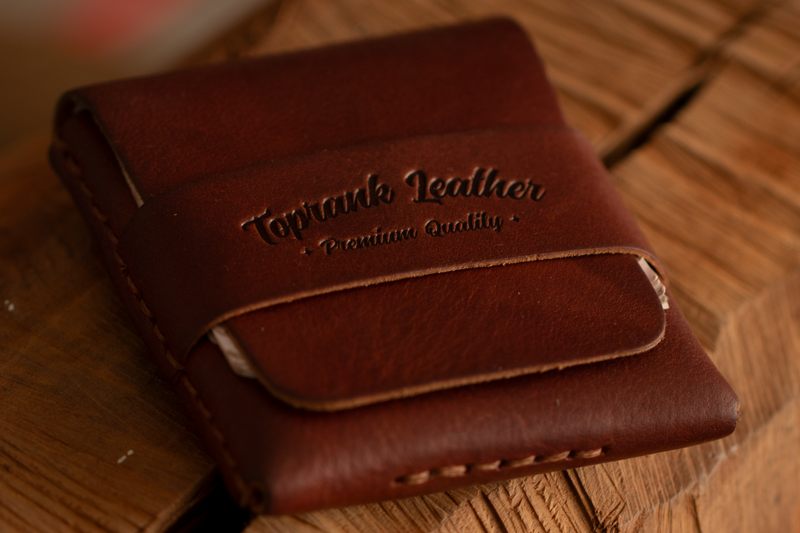Hand stitched full grain leather card wallet resting on a wooden workbench, its flap closed over a loaded card pocket