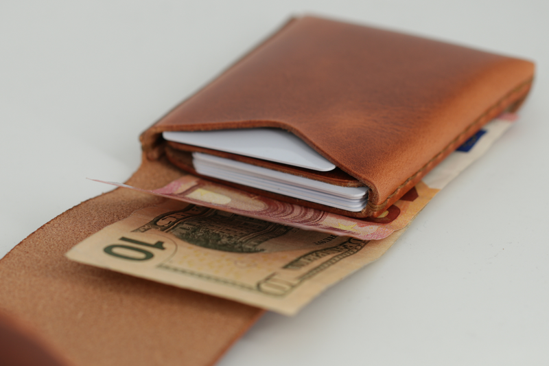 Open tan full grain leather wallet holding plain unmarked white cards and folded banknotes on a pale surface