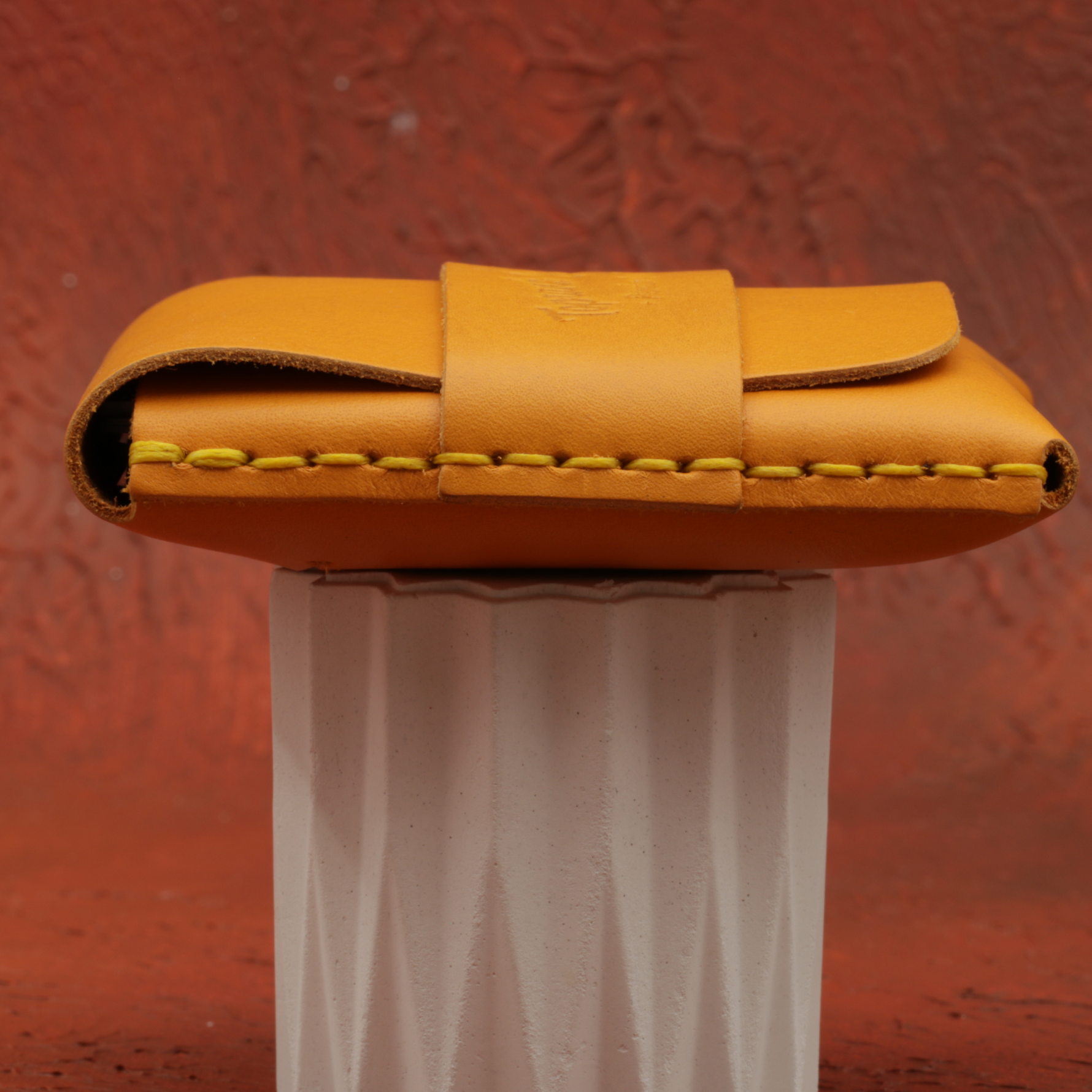 Yellow leather wallet on a white stand against a red textured background 