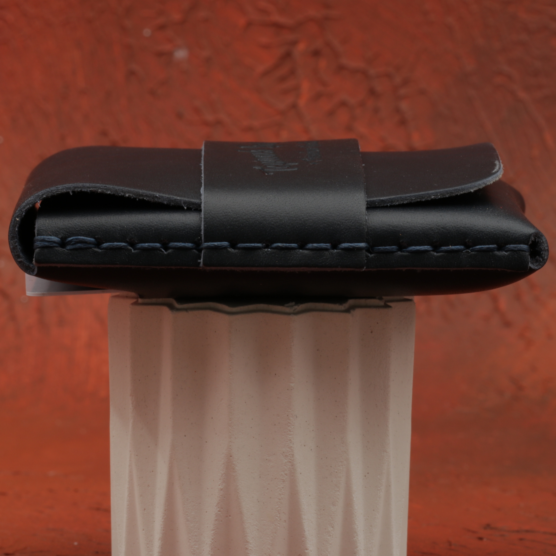 Black leather wallet on a stand against a red textured background 
