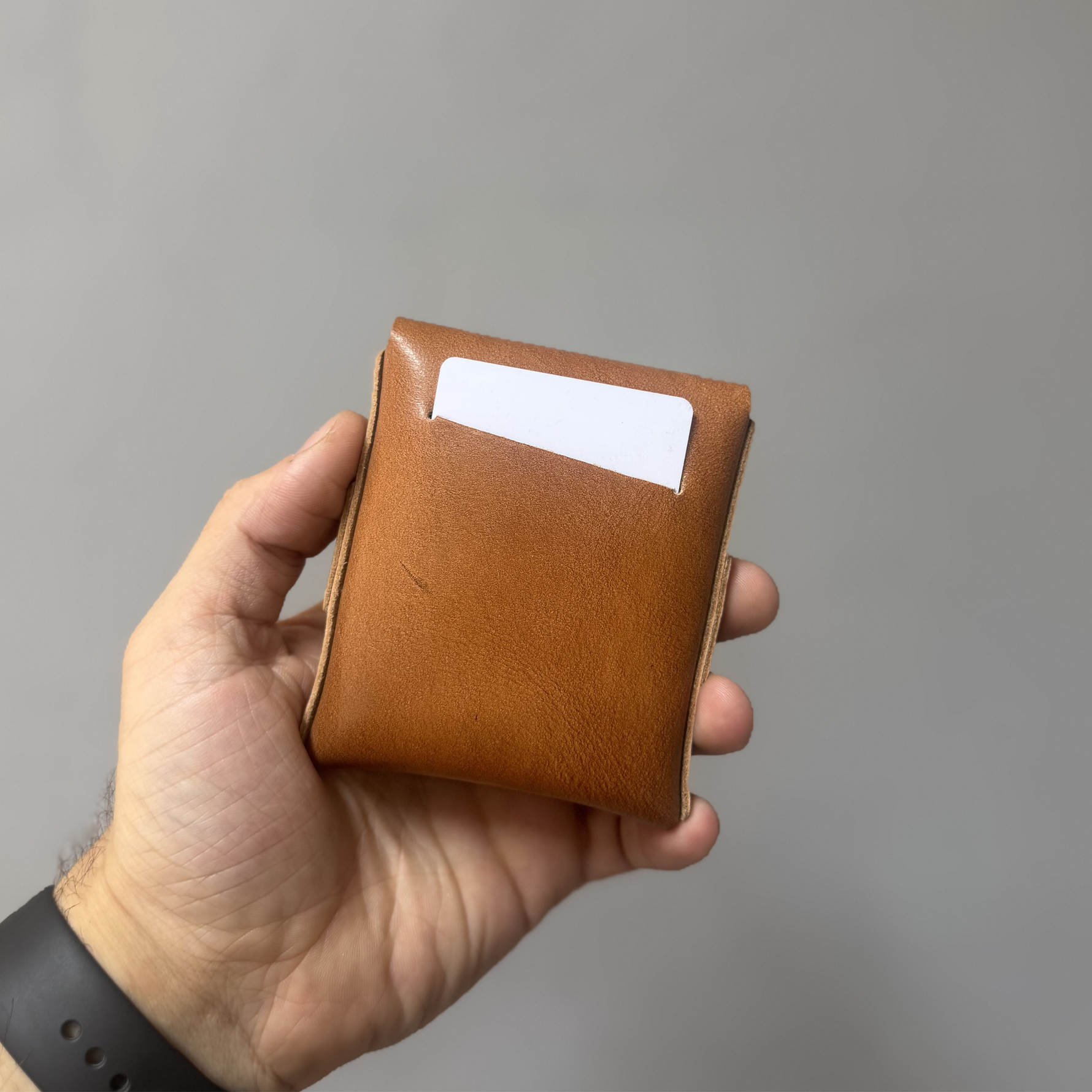 Hand holding a brown leather wallet against a gray background 