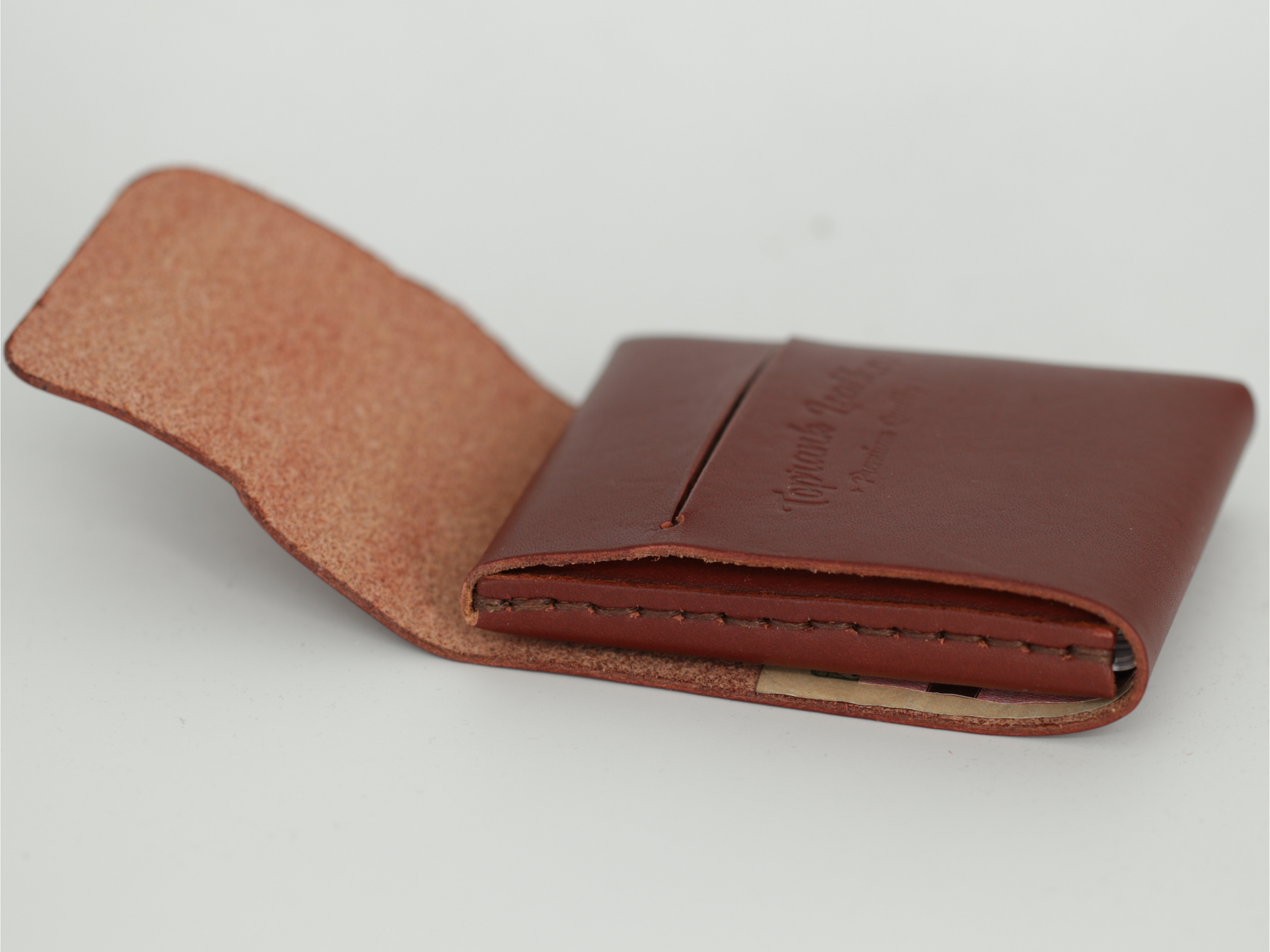 A brown leather card holder wallet shown open on a light gray background, with the interior lining visible and debossed branding on the front. 