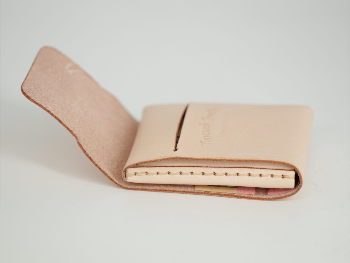 A light beige leather card holder wallet shown open on a clean white background, displaying its interior stitching and a small embossed logo. 