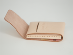 A light beige leather card holder wallet shown open on a clean white background, displaying its interior stitching and a small embossed logo. 