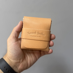 Hand holding a tan leather wallet with 'Toprank Leather' branding against a gray background 