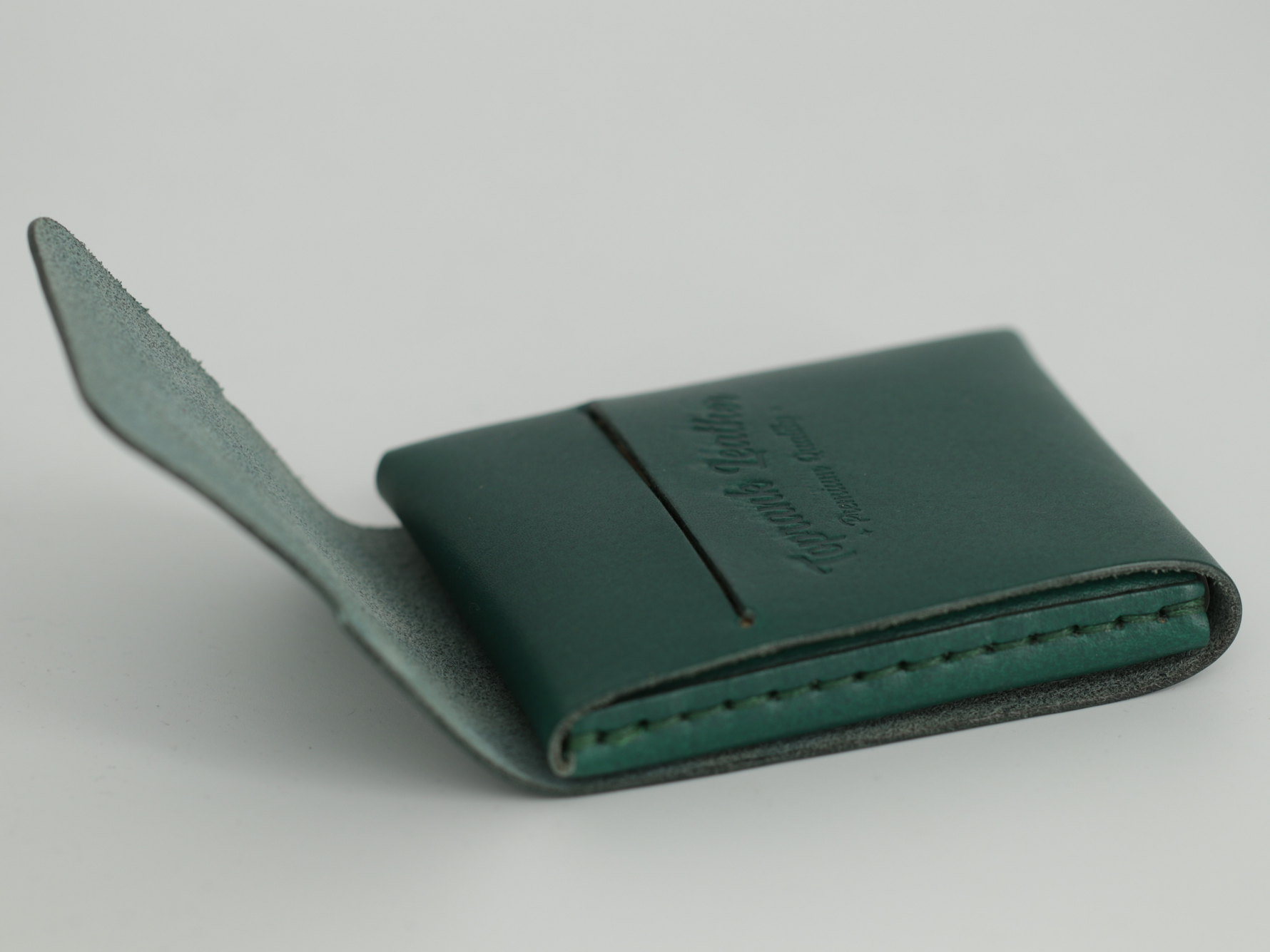 Gable leather flap wallet in Green shown closed at an angle, with the debossed logo on the flap. 