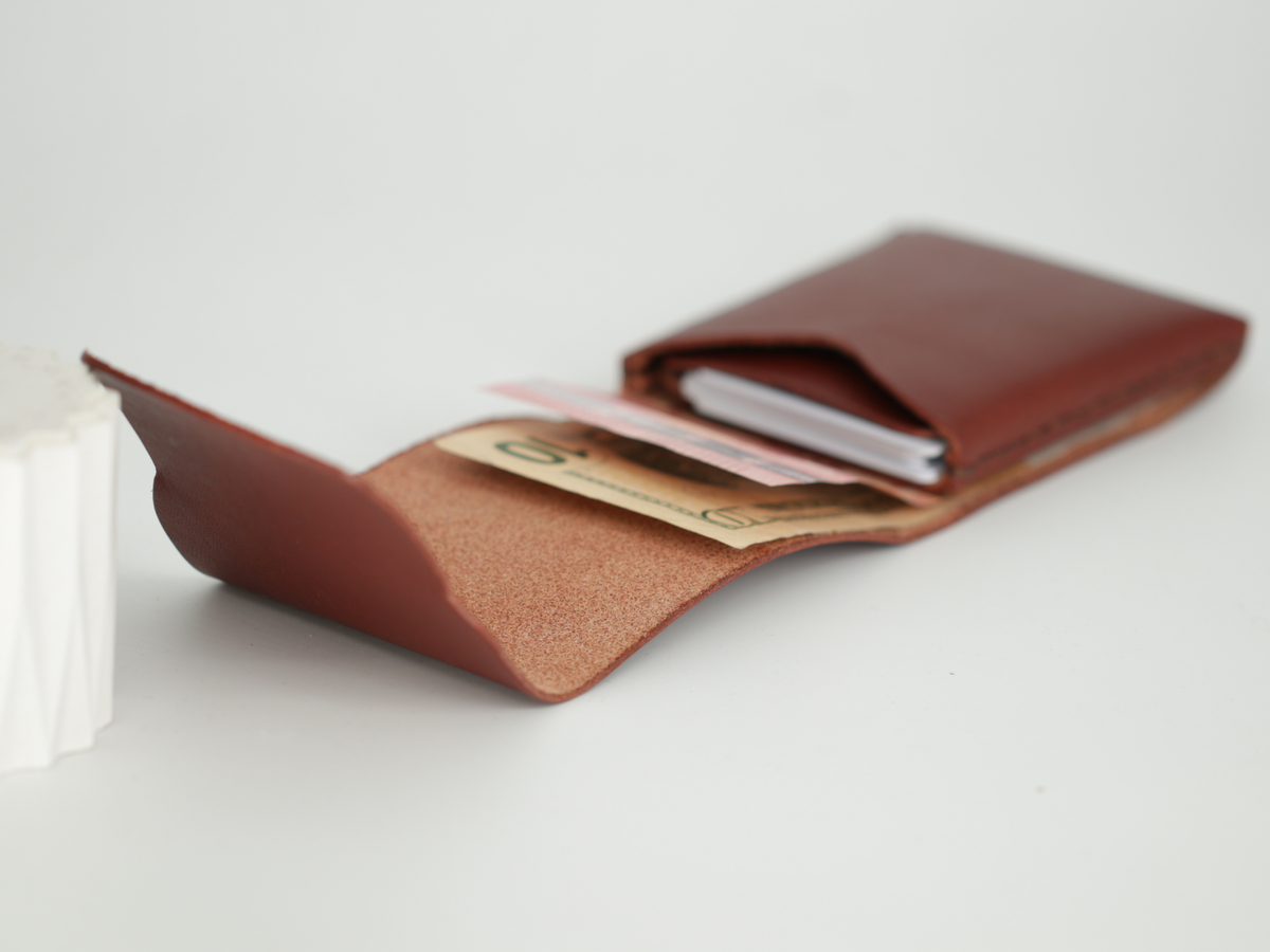 A brown leather card holder wallet shown open, containing credit cards and cash, on a light gray background. 