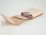 A light beige leather card holder wallet shown open, containing credit cards and a banknote, on a clean white background. 