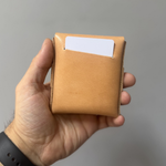 Hand holding a tan leather wallet with a card slot against a gray background 