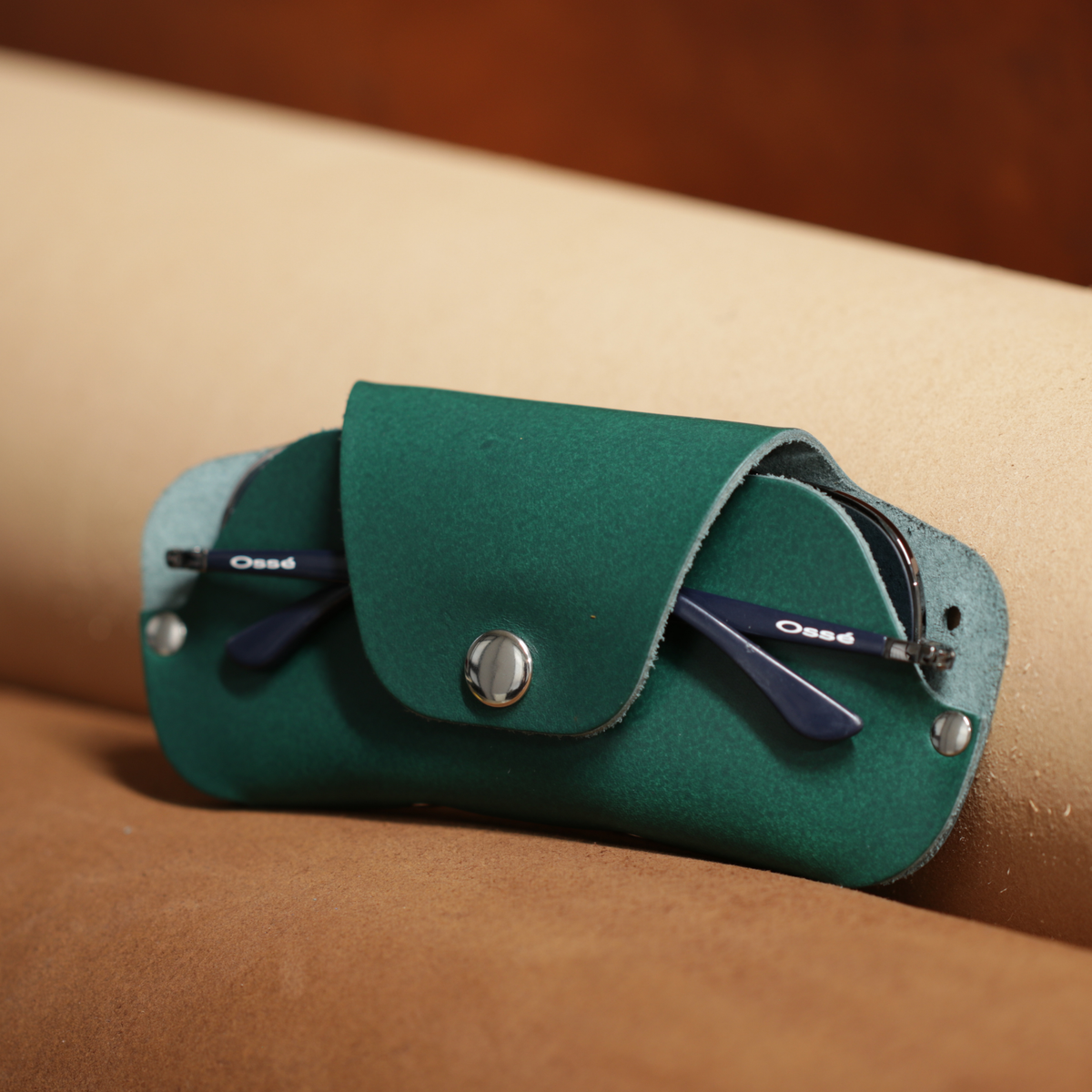 Green leather case with sunglasses on a beige surface 