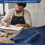 A man in a denim apron sits at a wooden workbench writing in a notebook beside a large folded piece of dark blue leather or fabric. Tools and sketch drawings are visible on the table and wall, with text banners reading 'MADE FOR MAKERS, NOT MASS PRODUCTION' and 'EASY TO CUT, PUNCH AND STITCH'. 