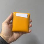 Hand holding a yellow cardholder with a white card on a gray background 