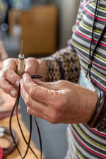 Close-up of hands working with a needle and thread, wearing a striped shirt. 
