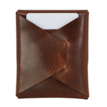 A brown leather card holder or sleeve with a diagonal fold design and a white card partially inserted, shown against a plain white background. 