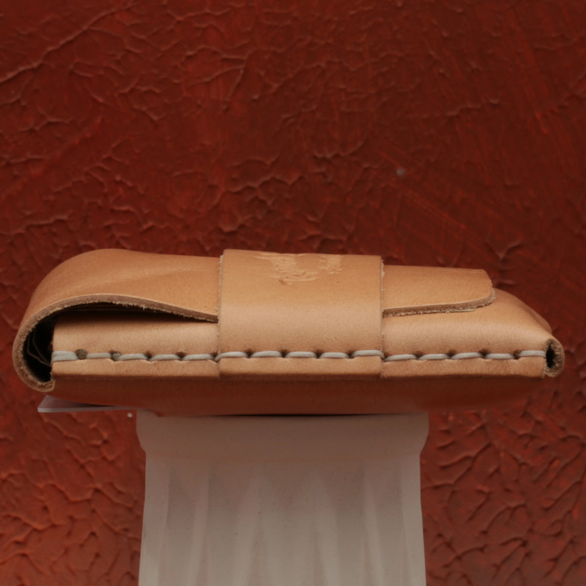 Brown leather wallet on a white stand against a textured red-brown background 
