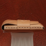 Brown leather wallet on a white stand against a textured red-brown background 