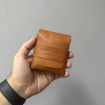 Hand holding a brown leather wallet with a visible brand logo against a gray background 