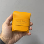Yellow leather wallet held in a hand against a gray background 