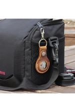 Black camera bag with a leather keychain on a wooden surface 
