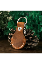 Brown leather keychain with metal ring on a pine cone against a green foliage background 