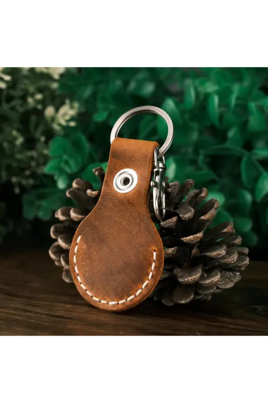 Brown leather keychain with metal ring on a pine cone against a green foliage background 