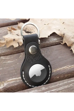 Black leather keychain with a metal ring on a wooden surface with leaves. 