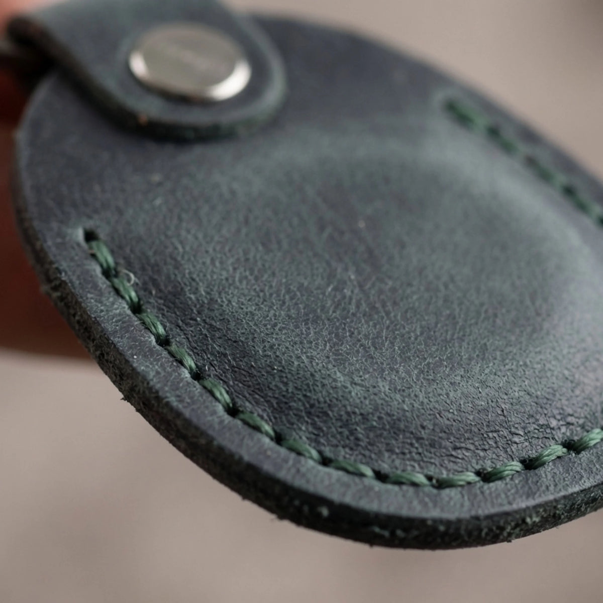 Close-up of a dark green leather key fob with stitching detail. 