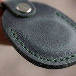 Close-up of a dark green leather key fob with stitching detail. 