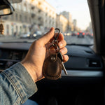 Hand holding a keychain with keys in a car, cityscape in the background 