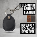 Black leather keychain with metal clip on a gray background, featuring text about full-grain leather and patina development. 